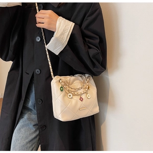 Detail of cream quilted bucket bag with colorful heart charms and woven chain strap