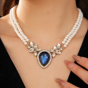 Vue macro du collier de perles double rang avec gemme goutte bleue et détails dorés
