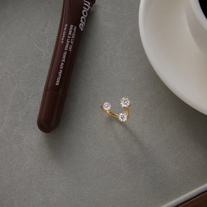 Detailed view of an open gold ring featuring three layered white zircons on a gray surface