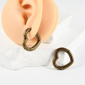 Detail of vintage heart earrings with gold scale texture on a silicone ear model