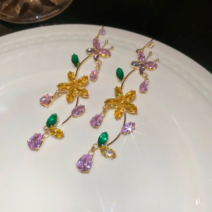 Macro detail of zircon butterfly and floral tassel earrings on a white ceramic plate