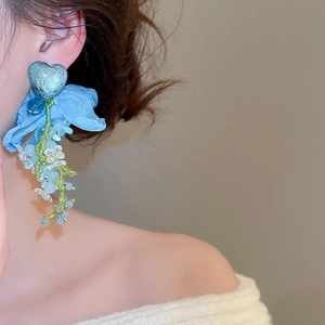 Detail of blue beaded tassel earring with heart stud and fabric flower on model