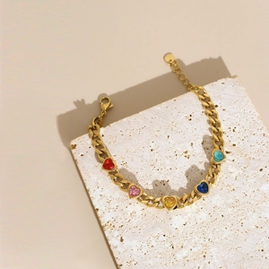 Gold Cuban chain bracelet with five colorful heart-shaped crystals on white stone podium