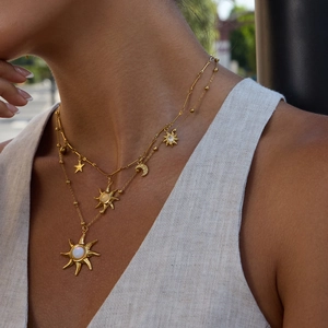 Detail of layered gold sun and moon pendant necklace worn by a model in natural light