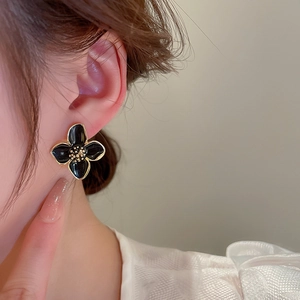 Detailansicht eines Models mit süßen schwarzen Emaille-Blumenohrsteckern mit Goldrand