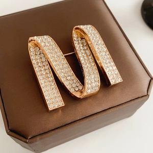 Macro shot of rose gold M letter brooch with sparkling diamonds on brown silk background