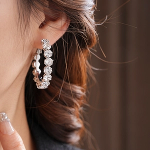 Close-up of model wearing large silver round hoop earrings with sparkling inset crystals