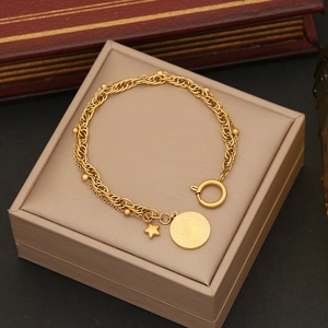 Detail of layered gold bracelet with coin pendant and star charm on a beige jewelry box