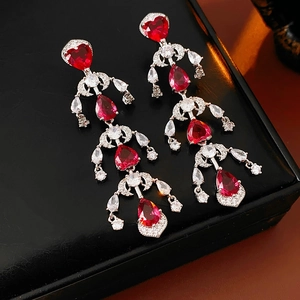 Macro detail of silver drop earrings featuring red heart gems and dangling crystal tassels