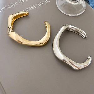 Detailed shot of gold and silver wavy irregular cuff bracelets on a grey book background