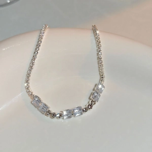 Macro shot of silver tennis necklace with rectangular zircon on white ceramic base