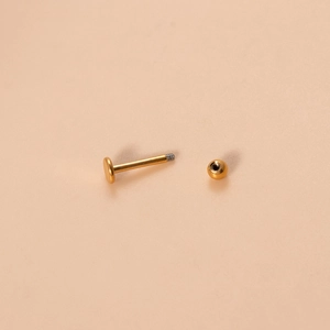 Detailed view of 16G golden titanium flat back stud piercing with ball screw closure