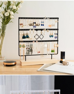 Three-layer black metal jewelry stand with wooden base displaying earrings on a desk