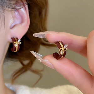 Close-up of C-shaped bow earrings with dark red matte finish and sparkling crystals