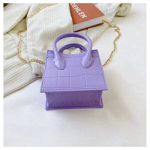 Detail of purple croc-effect mini bag with gold chain strap on a white surface