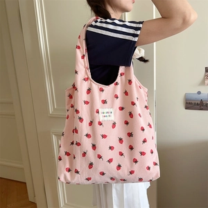 Détail du sac fourre-tout en velours rose à fraises porté par un mannequin en lumière douce