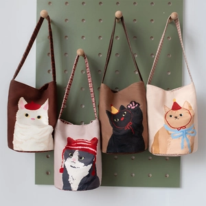 Minimalist canvas bucket bags with cute embroidered cats hanging on a display board