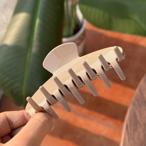 Close-up of a large beige acetate hair claw clip held against a natural outdoor background