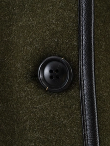 Close-up of wool texture with black leather trim and button on dark green coat
