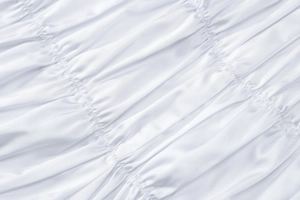 Close-up of premium white satin fabric with intricate pleated texture and glossy finish