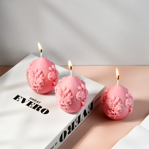 Detailed relief of pink rose flowers on egg-shaped candles with lit wicks
