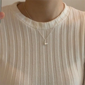 Minimalist V-shaped silver necklace shown on model wearing white textured sweater