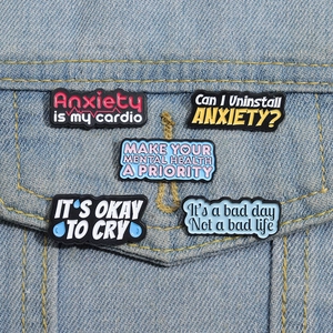 Close-up of five colorful enamel pins with mental health quotes on a denim jacket pocket