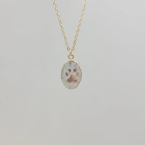 Detail of gold chain necklace with oval paw print pendant featuring natural stone texture