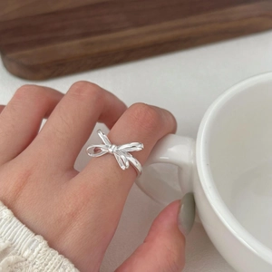 925 Sterling silver bow ring worn on hand holding a ceramic cup in a warm setting