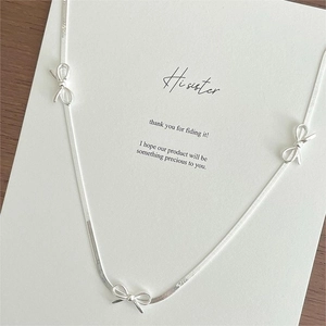 Macro view of silver snake chain necklace featuring three minimalist 3D bow pendants
