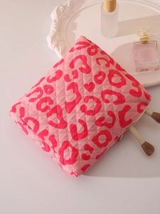 Pink quilted makeup bag with red leopard heart patterns next to brushes and perfume