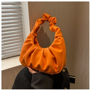 Close-up of vibrant orange ruched shoulder bag showing detailed PU leather texture