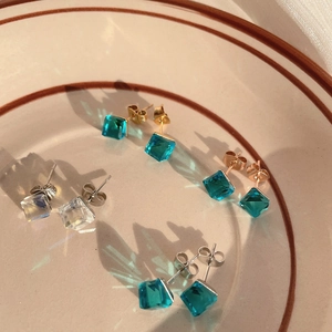 Macro shot of square cut crystal earrings reflecting colorful light on ceramic tray