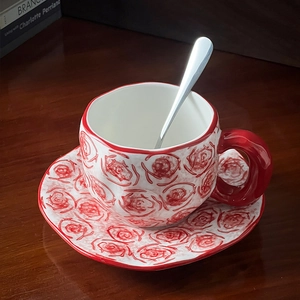 Close-up of hand-painted red rose patterns on ceramic coffee cup with a metallic spoon