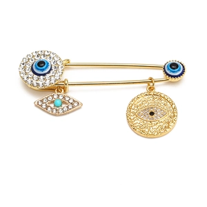 Detail of gold safety pin brooch with sparkling rhinestones and blue evil eye charms