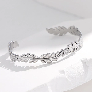 Bracciale rigido aperto minimalista in acciaio con motivo a foglie su base bianca