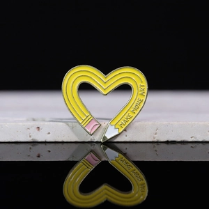 Detailed macro of yellow heart-shaped pencil enamel pin with Make More Art text
