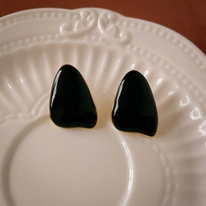 Detailed view of black enamel teardrop earrings with gold trim on a ceramic plate
