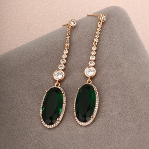 Macro detail of rose gold drop earrings featuring oval green stones and white zircons