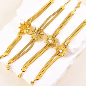 Double snake chain gold bracelets with sunflower and pearl charms on white stone