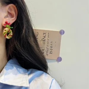 Close-up of model wearing handmade beaded Christmas wreath earrings with red bow accent