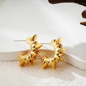 Detail of 18K gold C-shaped sunburst earrings on natural stone and wood background