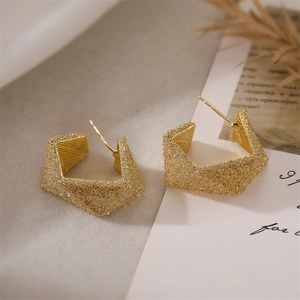 Macro shot of geometric gold hexagon earrings featuring a stardust brushed metal finish