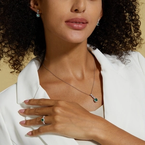 Elegant emerald jewelry set with necklace, ring and earrings on model in white suit