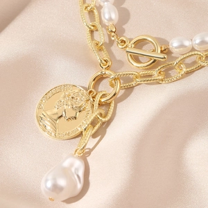 Close-up of layered necklace with baroque pearl, coin pendant and golden OT clasp detail