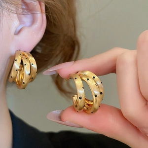 Dettaglio di orecchini a C a tre strati placcati oro 18k con pois neri e finitura opaca