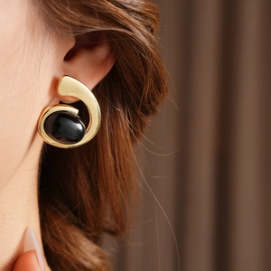 Detail of geometric gold earrings with black stones worn on a model against a soft fabric