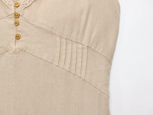 Détail macro d'une robe midi en lin beige avec boutons marron et plis à la taille