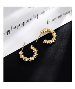 Macro shot of gold textured C-shape stud earrings with dense grainy metallic finish