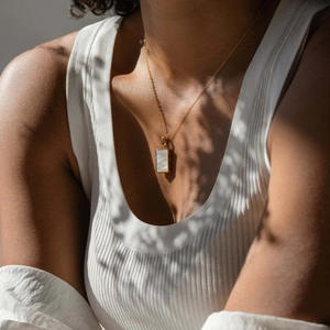 Golden rectangular necklace with white shell pendant shown on a model for display